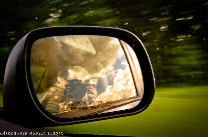 clouds and camera reflected in the side-view mirror of the moving car