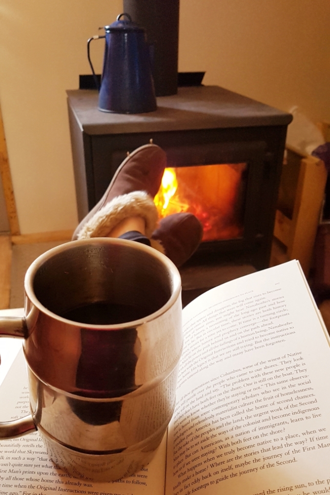 coffee and book in front of a wood stove